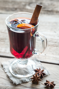 Clear glass of mulled wine with a cinnamon stick and fresh orange slice.